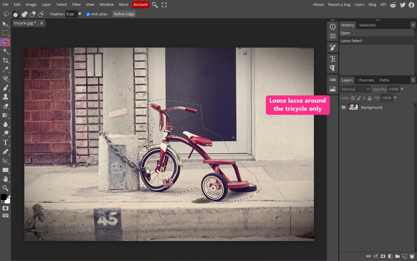 A loose lasso selection drawn around a red tricycle, leaving the red brick wall outside it